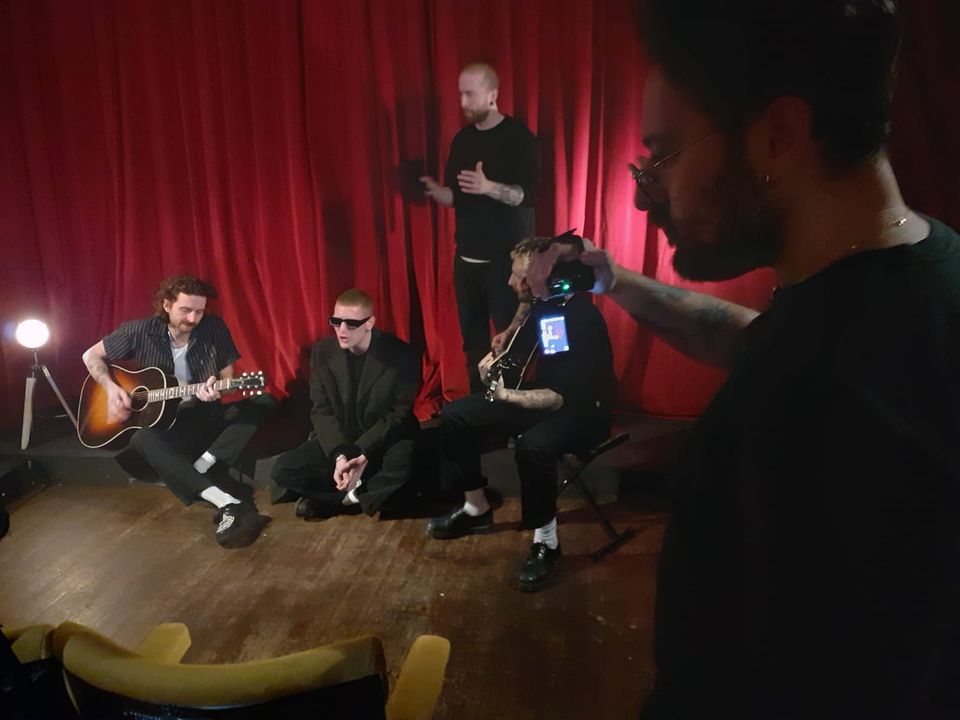 Kid Kapichi band sitting at front of cinema. 4 men with instruments sitting in front of velvet curtain